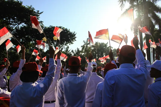 A crowd in white shirts and red caps waves Indonesian flags in the sunlight