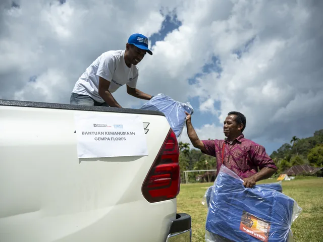 A volunteer hands a tarpaulin package down from a pickup to a resident at the Flores earthquake response